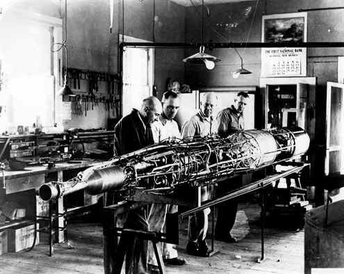 The 1940 Goddard rocket on its assembly frame, with the combustion chamber on the left and oxygen and gasoline tanks ton the right. In the photo: Dr. Goddard (left) with assistants N.T. Ljungquist, A.W. Kisk, and C.W. Manjur.
