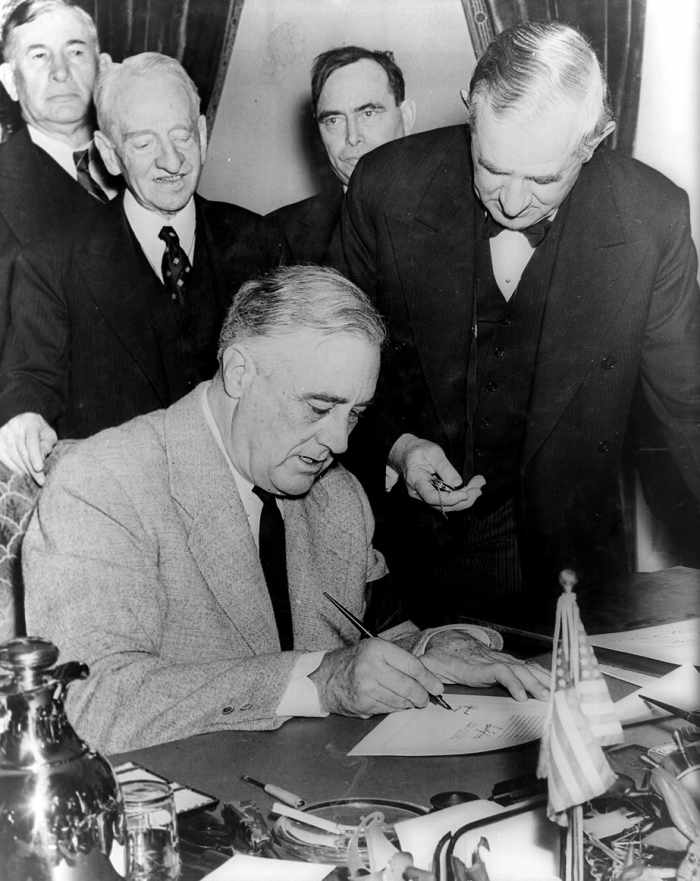 12/11/1941 - United States President Franklin D. Roosevelt signing the declaration of war against Germany, marking US entry into World War II in Europe. Senator Tom Connally stands by holding a watch to fix the exact time of the declaration.