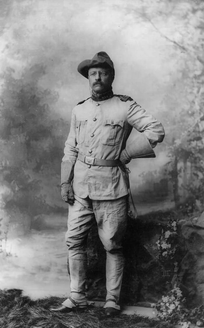 Colonel Theodore Roosevelt, in rough rider uniform, full-length portrait, standing and facing slightly left.