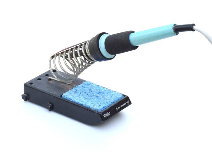 Typical electric soldering iron on a stand. The blue sponge is used for removing flux residue from the tip of the iron.