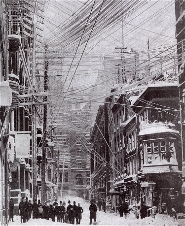 Photograph of a tangle of telephone, telegraph, and power lines above the streets of New York City after a major snow storm in 1888.