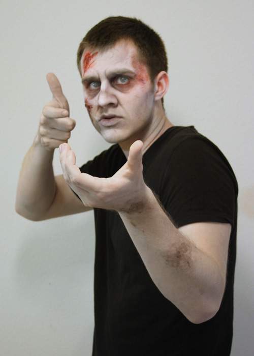 The left hand is held in the 'C' hand shape facing upwards while the right hand is held near the face with the index finger out and bent as if resting on a trigger; the thumb extended.
