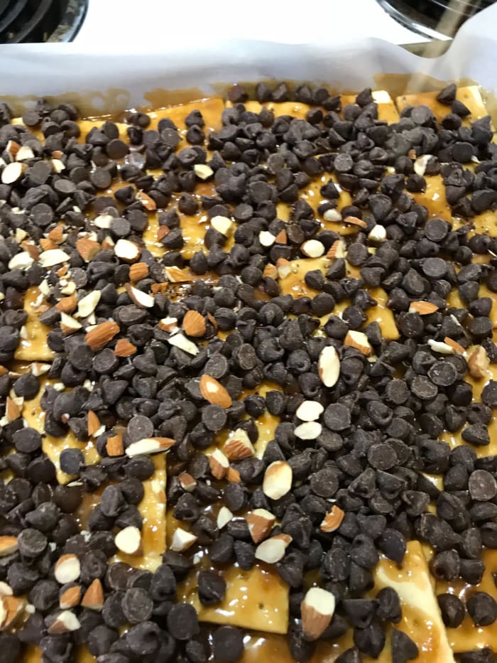 When the hot toffee comes out of the oven, immediately sprinkle on chocolate chips. This melts the chocolate so you can spread it. Sprinkle the almonds on top and let it sit for a couple of minutes to soften the chocolate chips to spread-ability.