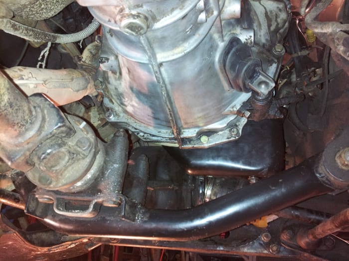 Transmission with hydraulic clutch cylinder installed. The crossmembers are the front differential which tucks up beneath the oil pan. The engine cannot be pulled forward until the differential is lowered or removed. Transmission drain plug visible
