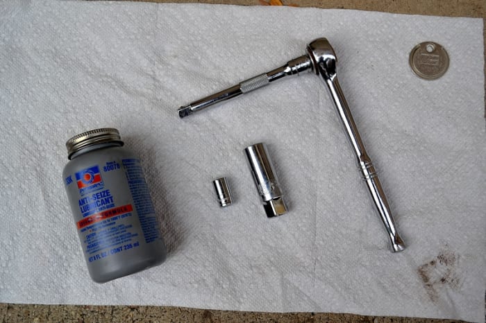 The tools, from left to right: bottle of anti-seize lubricant, a 10mm socket, a 5/8 inch spark plug socket, a 3/8 drive ratchet with a 5 inch extension bar, and a spark plug gap tool coin.