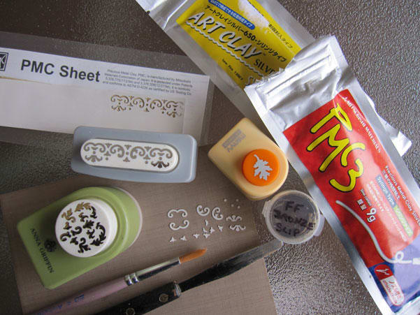 Metal clay syringe, metal clay slip, palette knife, brush and PMC Sheet appliqué cutouts made with paper punches