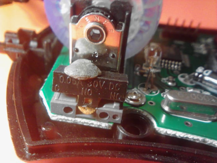 Notice the small gray material that looks like putty on top of the switch. This is sticky material for hanging posters on walls. It is holding the small white piece of the switch so it won't be lost when we take apart the switch.