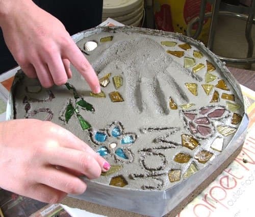 Step 7. Using a pencil or thin stick, carve any letters/numbers into the mortar. Transfer your glass and other decorative items to the wet mortar gently pressing each piece into the wet cement. Allow the mortar to dry (set-up) for about 15 to 20 min