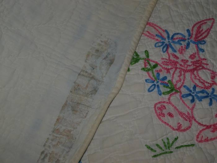 Antique quilt with damage from adhesive tape used to hang the quilt. The tape was removed but the glue remained, as well as the tear that occurred when removing the tape.