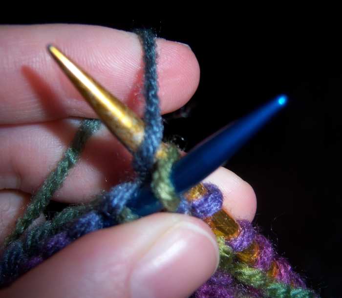 Instead of letting the stitch slip from the blue needle, insert the gold needle through the loop of yarn behind the blue needle and knit one stitch.