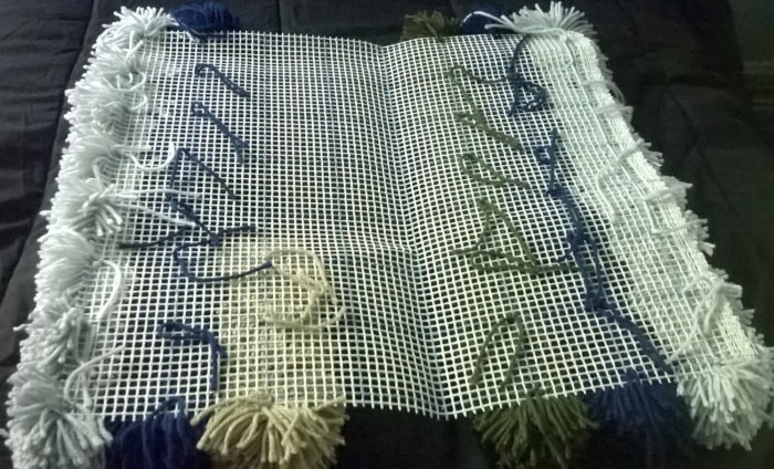 Bottom of yarn pom pom rug in progress. Your rug will look something like this while you're tying the pom poms to it.