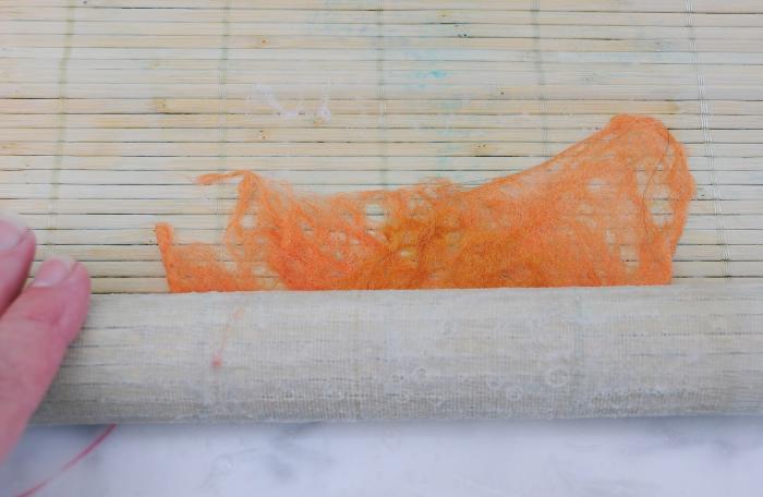 Roll in a sushi mat, alternating the direction in which you lay the circles of wool