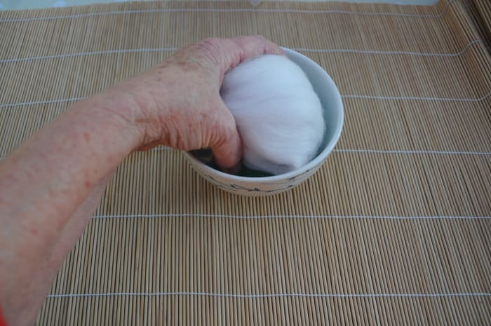 Wet all sides of the wool covered polystyrene ball by dipping each side lightly into the hot soapy water.