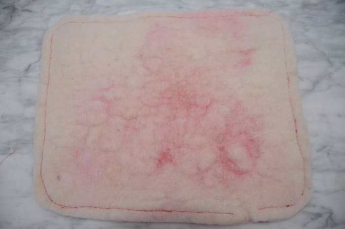 The back of the heart shaped cushion showing how red the white wool looked even after needle felting. The front is now snow white.