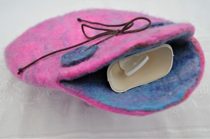 The filled hot water bottle seen inside the wet felted cover. The water bottle is held in very securely by the leather strips.