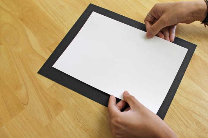 Center the white paper on the black and glue. The black becomes your frame, and the white becomes your mat.