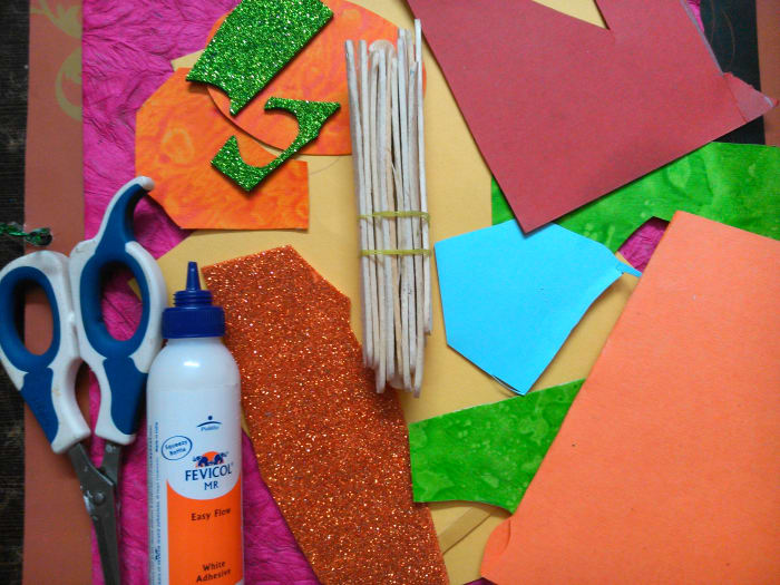 Acrylic paint, a brush, six ice cream sticks, a glue stick, scissors, a few sheets of colored, textured, and shiny paper.