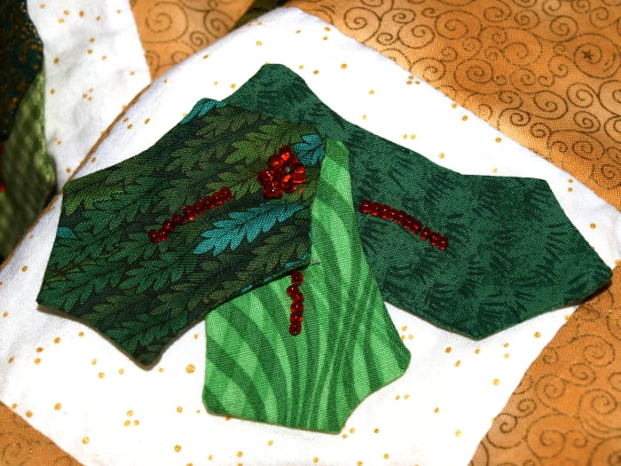 Fabric and beads combine to make a nice dimensional holly leaf embellishment on a Christmas quilt.