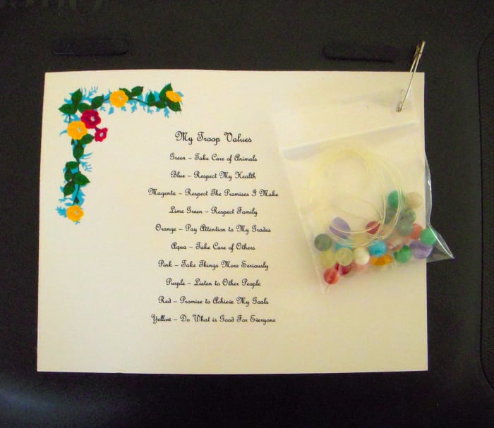 Troop values are represented by different colored beads. A pre-printed card that explains the meaning and value of each bead color is a part of this SWAP. Pin a small zip bag containing stretchy jewelry cording and beads.