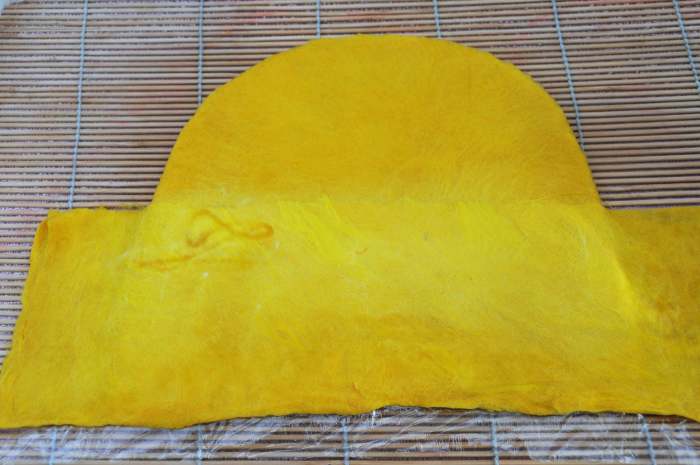 A piece of pre-felt covering the cling wrap, fibers extending above and onto the hat below.