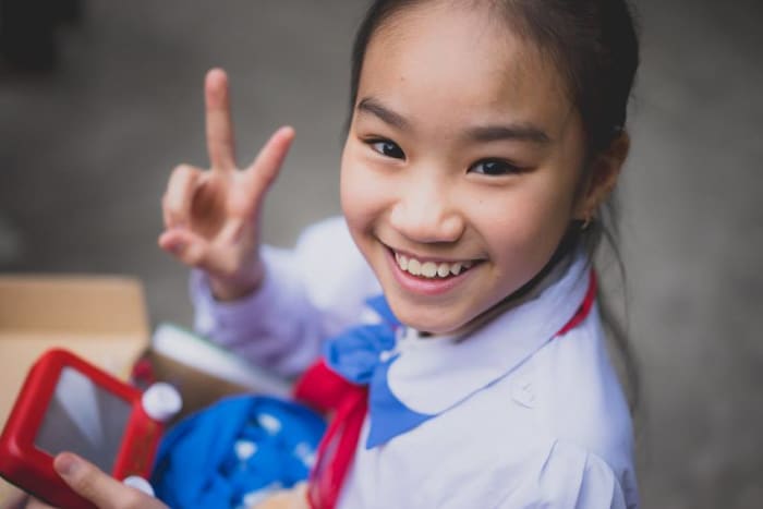 A girl holds up a peace sign while playing with the Etch-a-Sketch from her shoebox.