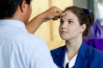 A member of the clergy applying ash in the form of a cross to a woman's forehead.