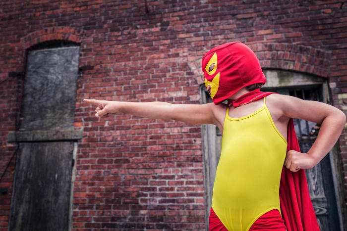 A young man wearing a red hood with a stitched mask, a red cape, red leggings, and a yellow body leotard representing his favorite super hero.