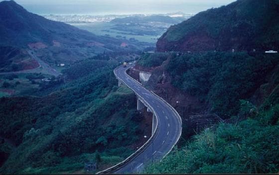 An aerial view of the highway to the windward side of O'ahu on the way to the North Shore, with Kane'ohe and the blue Pacific Ocean beyond.