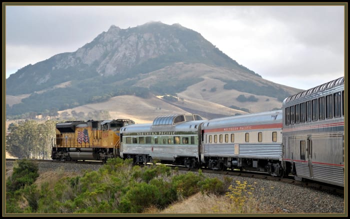 Bishops peak from the Coast Starlight The yellow Union Pacific Locomotive is helping push this longer than usual train around Cuesta curves and up the grade .