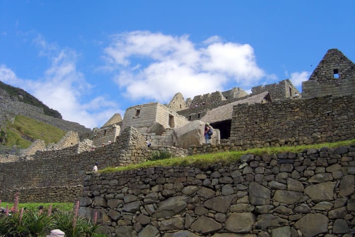 Looking upward past the masterfully constructed stone walls of Machu Picchu to the brilliant blue sky adorned by a few clouds.