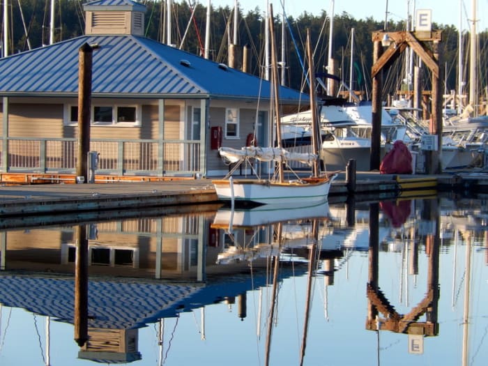 A modern restroom building with showers at the Friday Harbor Marina, with a classic sailing vessel reflected in the water alongside.