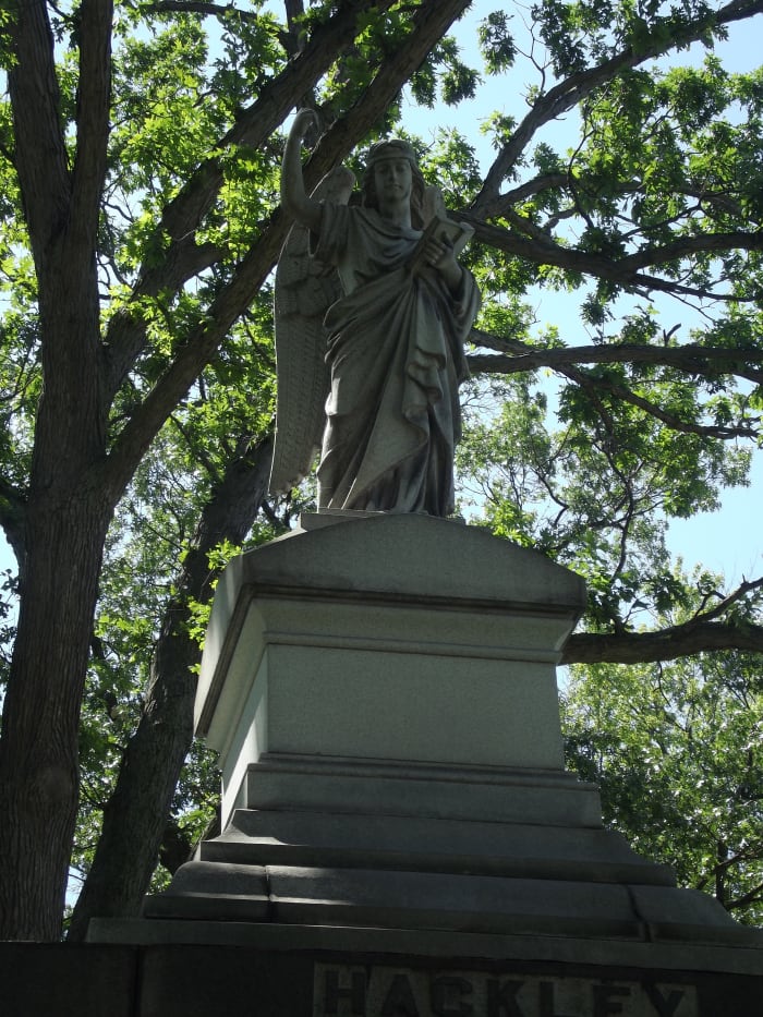 The angel at the top of the Hackley monument. The angel has its wings folded back and is pointing upward while the other holds a book close to the angel's body. Evergreen Cemetery, Muskegon, MI.