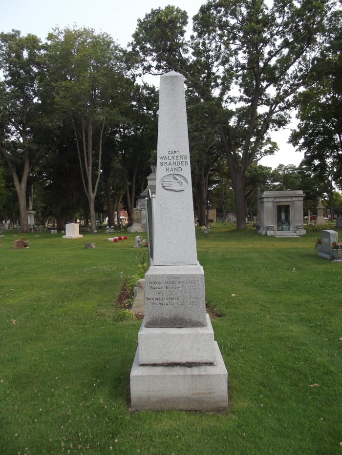Obelisk grave marker of Captain Jonathan Walker. Monument is marked with an engraved relief of a man's hand branded with SS and the text "Captain Walker's Branded Hand." Evergreen Cemetery, Muskegon, MI.
