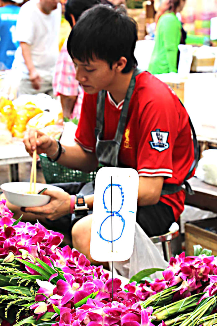 A flower seller pauses to enjoy lunch. The flowers are that most traditional of Thailand blooms - pink-purple orchids