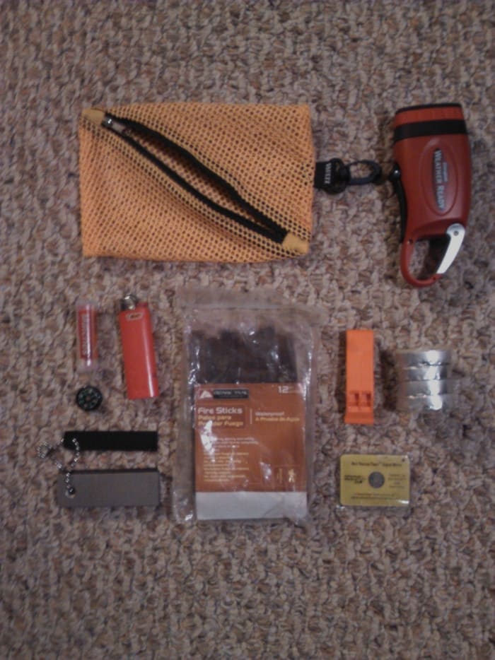 From left to right: crank flashlight, waterproof matches, lighter, flint with striker, fire sticks, whistle, tealights and signal mirror.