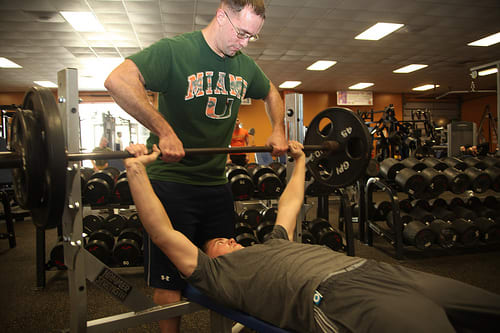 The bench press is the ultimate in upper body strength. Here we see great form - a spotter, flat back, feet on the floor and arms not locked out.