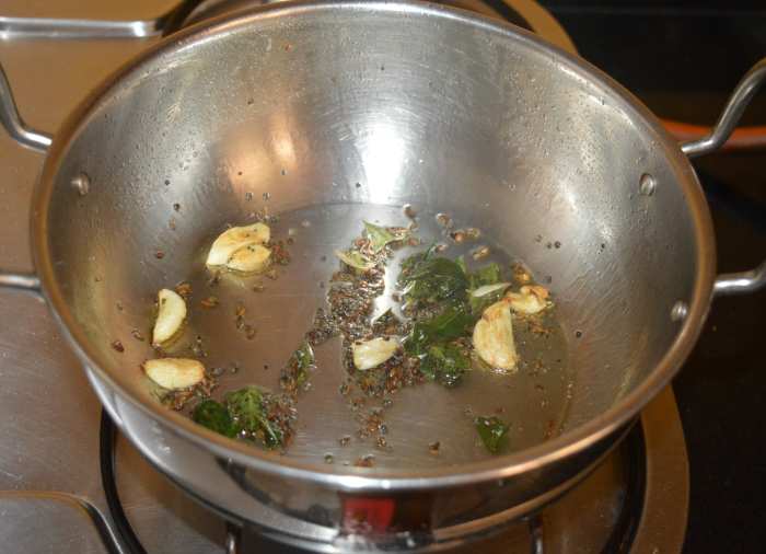 Step two: Heat oil or ghee in a deep-bottomed pan. Add mustard seeds and allow them to crackle. Add cumin seeds, curry leaves, and slightly crushed garlic cloves. Continue to saute until the garlic becomes golden brown.