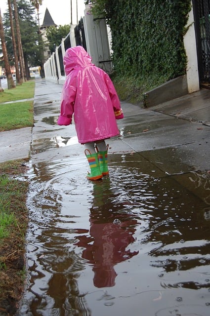 A child wears her matching pink and green rain gear on a very wet day.