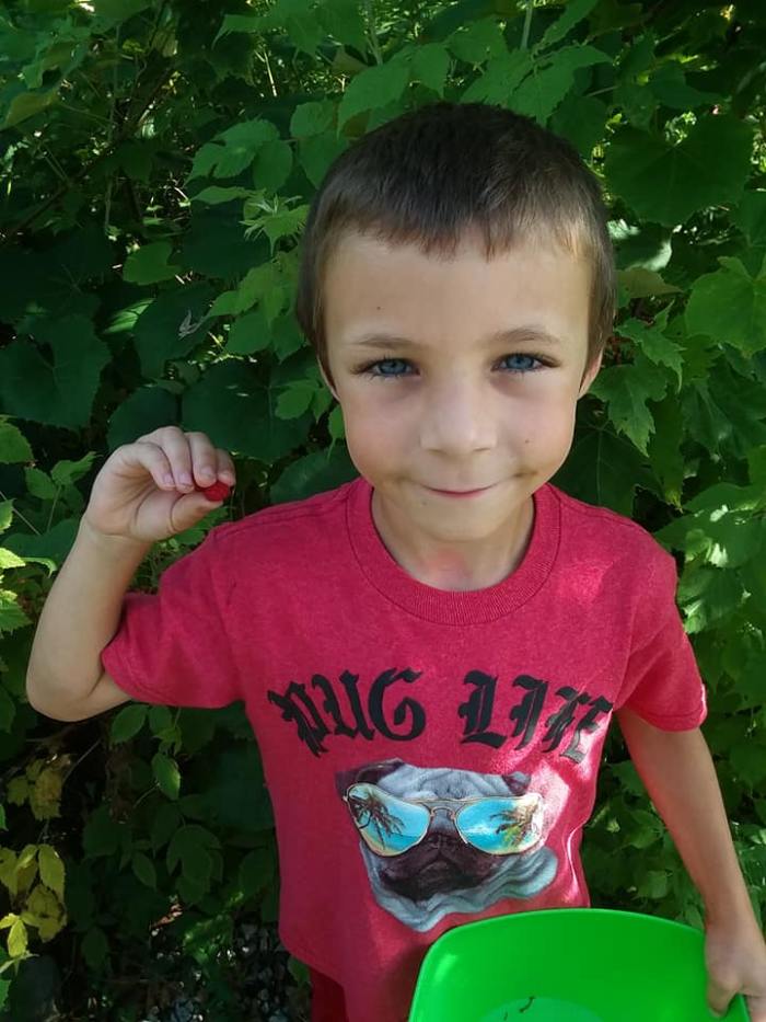 Lucas with a raspberry and his eyes are the same color of the blueberries almost purple.
