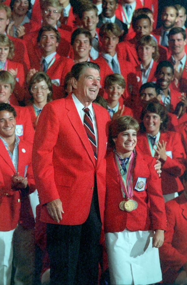 Perky Mary Lou Retton was one of America's darlings for the gymnastics team. Posing here with President Ronald Reagan who towers over the 5'2" star as the US Olympic Team looks on.
