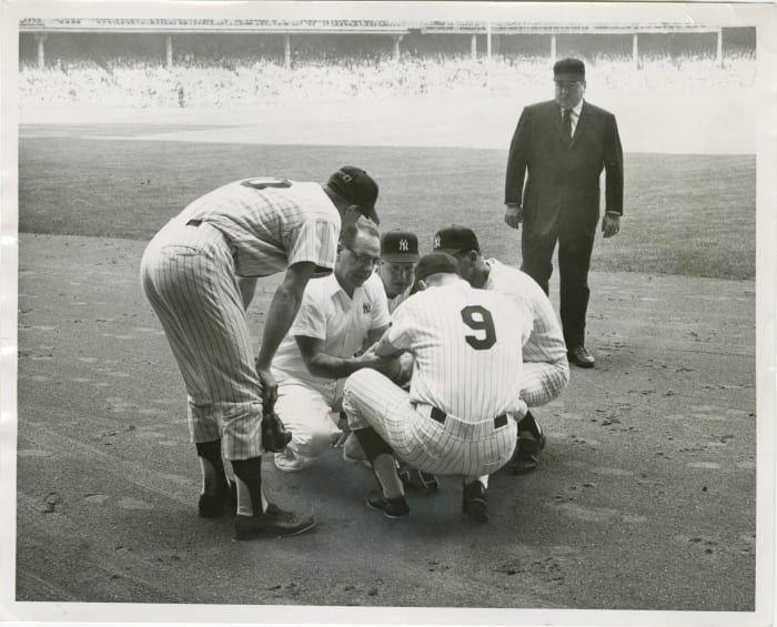 3rd inning, Game 2: Roger Maris is being checked out by the trainer and Houk. Joe Pepitone and umpire John Rice look on.