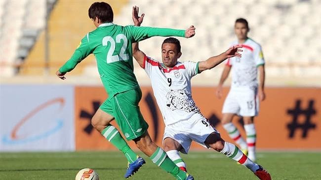 Seldar Geldiyev of Turkmenistan (22, green) attempts to evade a tackle from Omid Ebrahimi (9, white) during a 2018 FIFA World Cup qualifier on November 12, 2015 in Tehran, Iran. The match, played at Azadi Stadium, ended 3-1 to Iran.