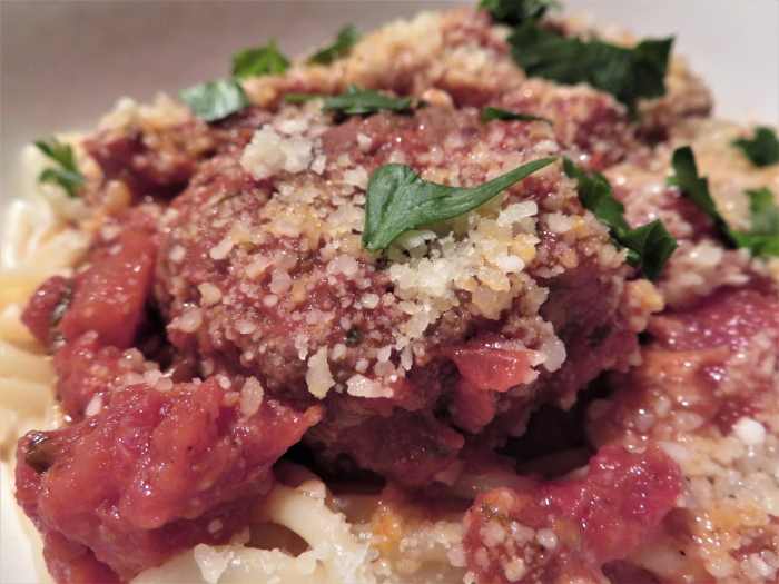 Completed dish with meatballs and sauce served over spaghetti and topped with grated Parmesan and chopped parsley.