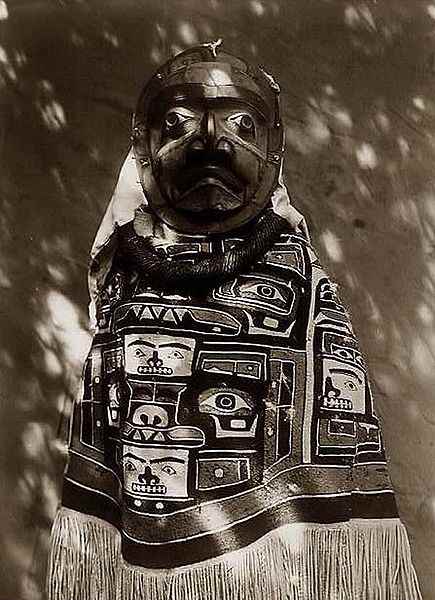 From Alaska, this is a woman in a fringed Chilkat blanket, a Hamatsa neck-ring and a mask representing a deceased relative who had been a shaman.