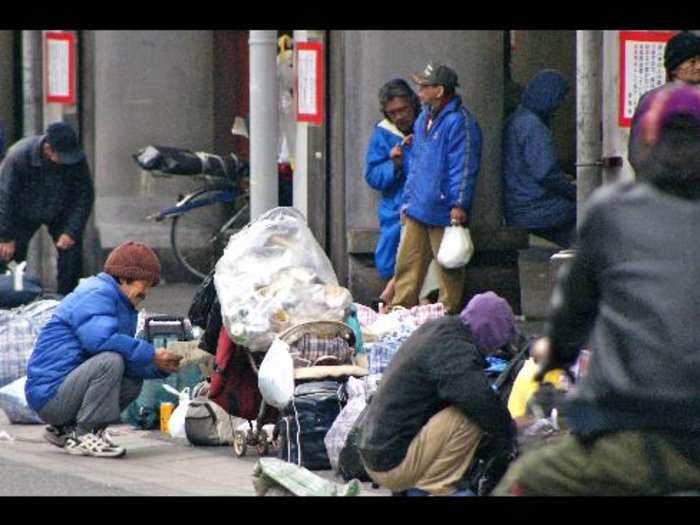 A stream of homeless men arriving at the area's largest shelter in Airin's dirt covered park; these men with greying hair and thick coats warming themselves, around a fire as others rummaged through the piles of trash, in Japan.