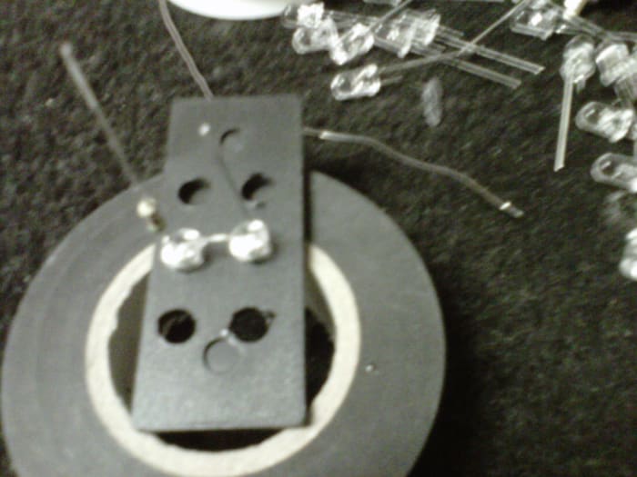 End of the box, drilled with a pair of LEDs ready to solder. You are soldering the - end of the one with the resistor to the + end of the other. Thus the pair's positive end has a resistor and negative end is just a lead.