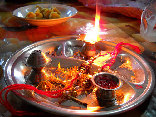 rakhi thali with diya (lamp), roli (red tilak in the cup), rakhi or mouli, sweets in another plate far end, incense stand, flowers