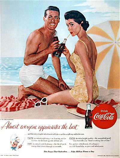 boy and girl on a beach both sipping a Coca Cola via straws with a striped yellow beach umbrella