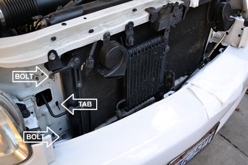 Remove the bolts holding the radiator in, there are 4 total with 2 on each side (only 2 are visible in this photo). The Tabs will hold the radiator in place even when the bolts are removed.