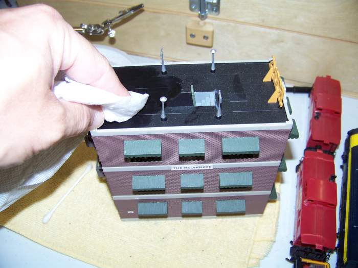 I use damp paper towels to clean buildings. Water does not seem to affect the dried acrylic paint I use.
